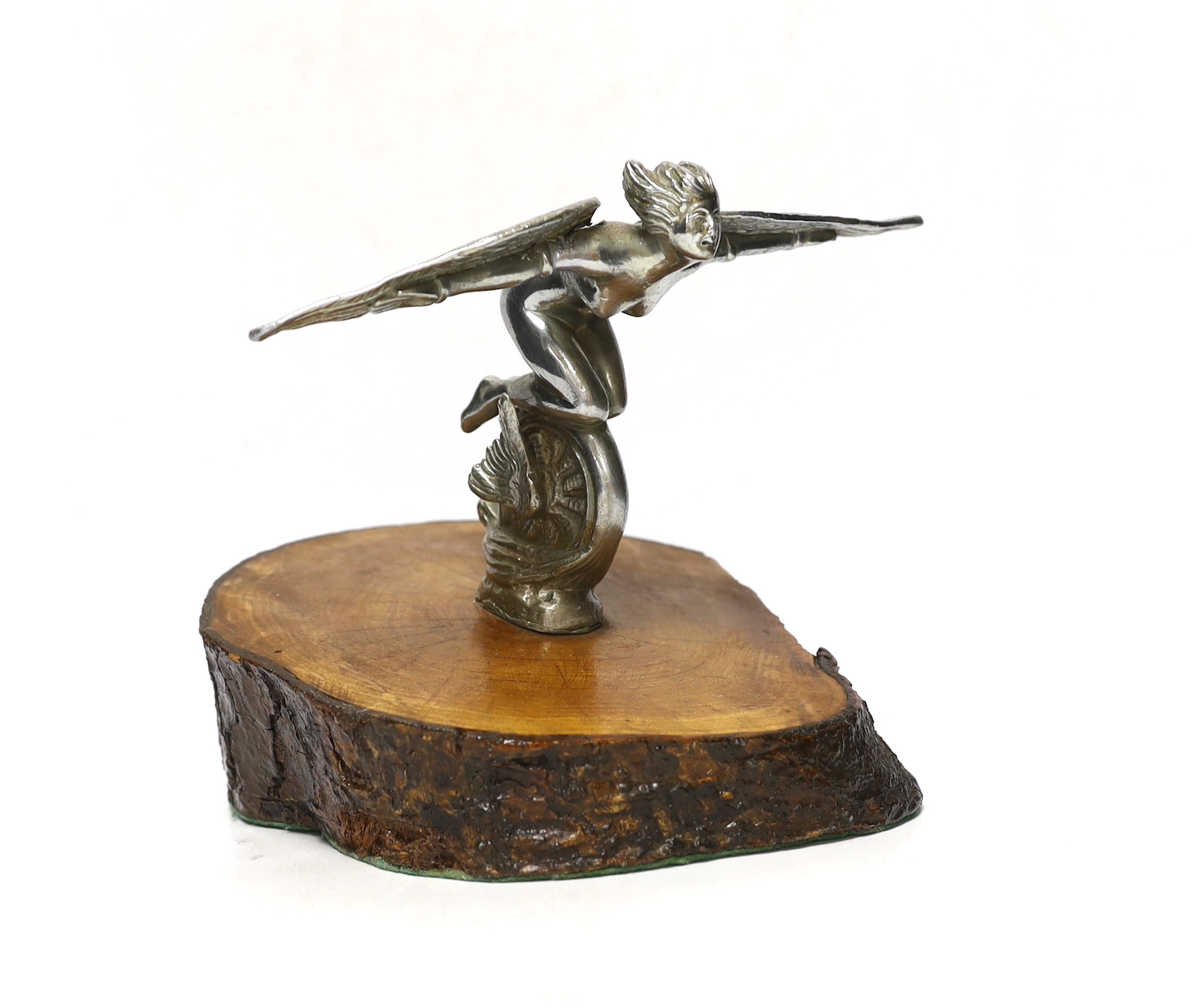 A vintage chrome plated car mascot of a winged female riding a wheel, mounted on a tree trunk cross-section, 19cm high